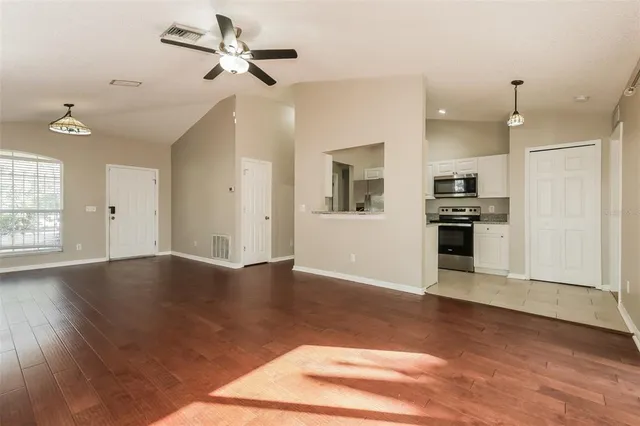 an empty room with wooden floor a ceiling fan and kitchen view