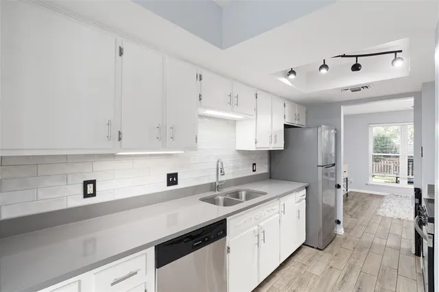 a kitchen with a sink stainless steel appliances white cabinets and wooden floor