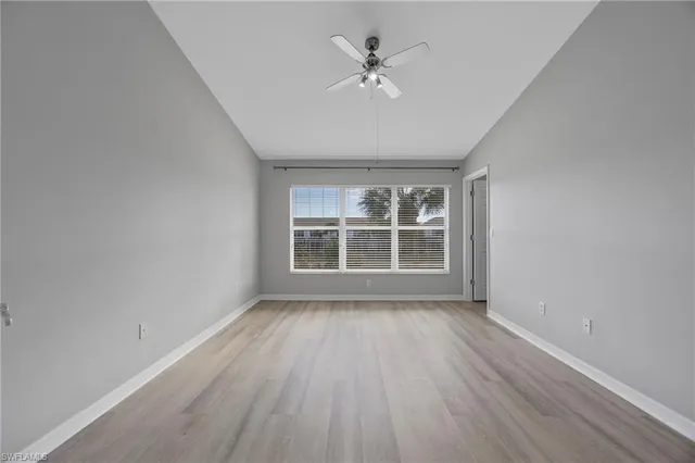 an empty room with wooden floor chandelier fan and windows