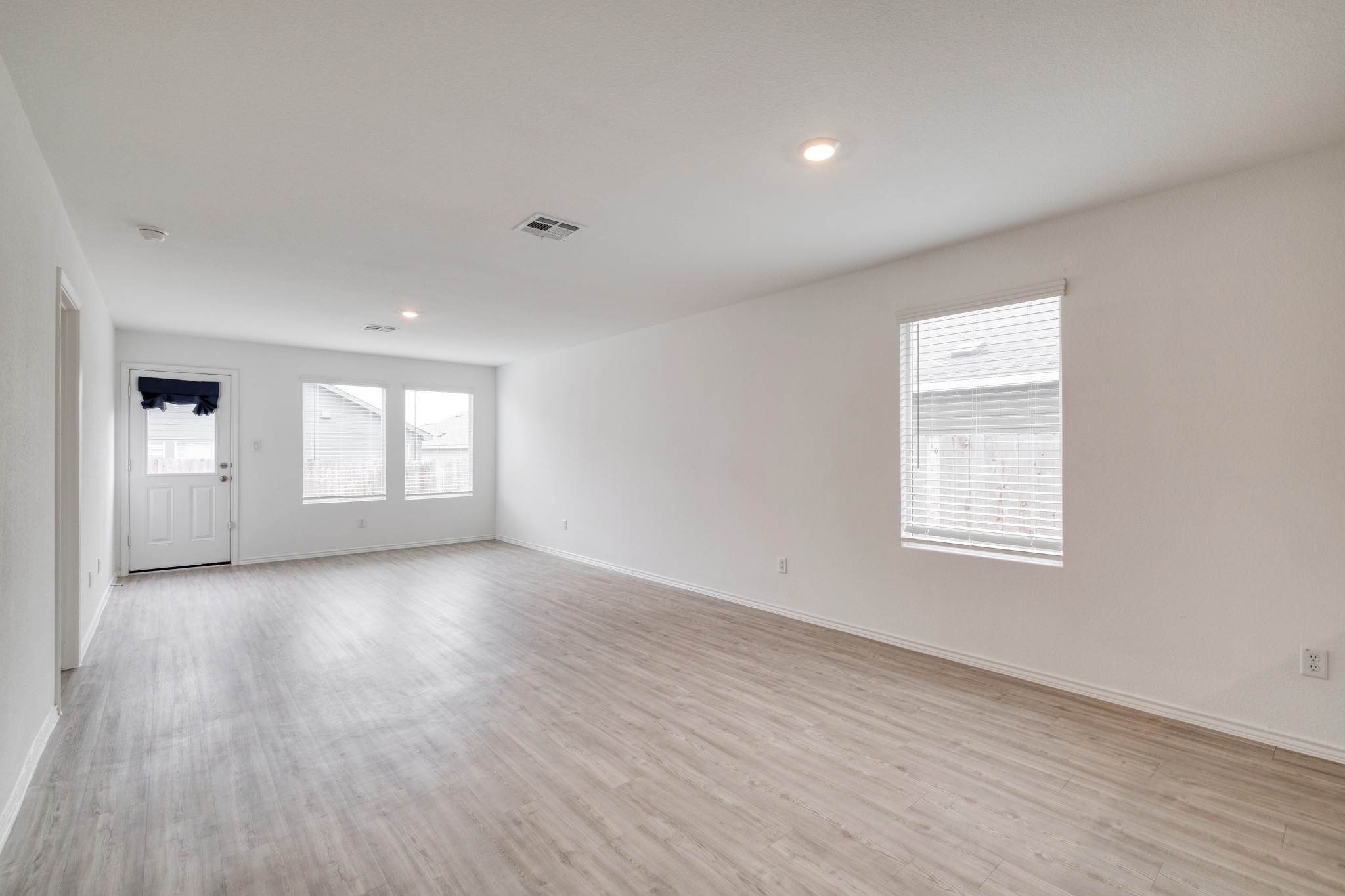 23412 Tiny Moons Way Elgin, TX 78621 - Photo 13 of 38 Spacious room featuring wood-finish flooring, white walls, multiple windows with blinds, recessed lighting, and a rear exit door