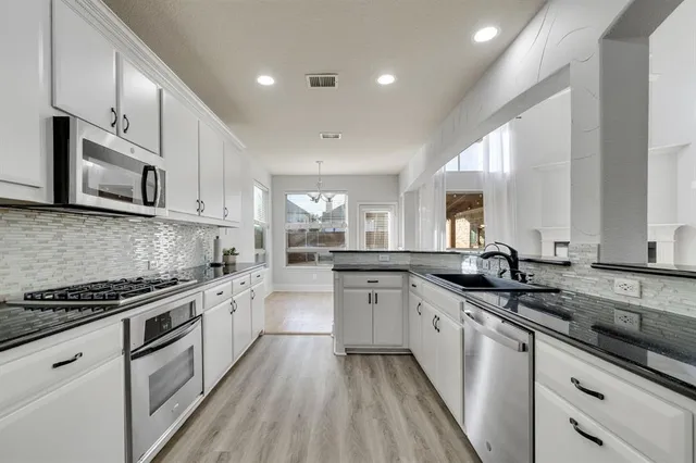 a kitchen with granite countertop white cabinets white appliances a sink and dishwasher with wooden floor