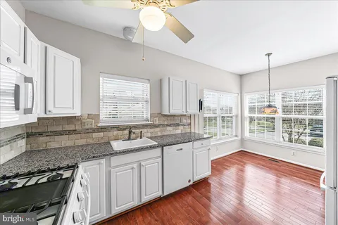 a large kitchen with granite countertop a stove a sink a window and wooden floor