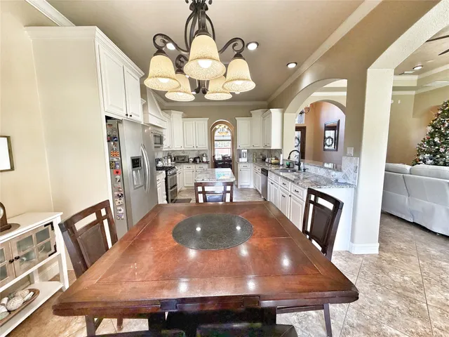 a white kitchen with stainless steel appliances granite countertop a stove top oven a sink a dining table and chairs with wooden floor