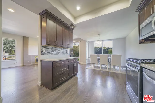 a kitchen with stainless steel appliances granite countertop a stove top oven a sink dishwasher and a dining table with wooden floor