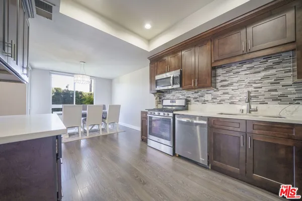 a kitchen with stainless steel appliances granite countertop wooden cabinets a sink dishwasher a stove and a refrigerator with wooden floor