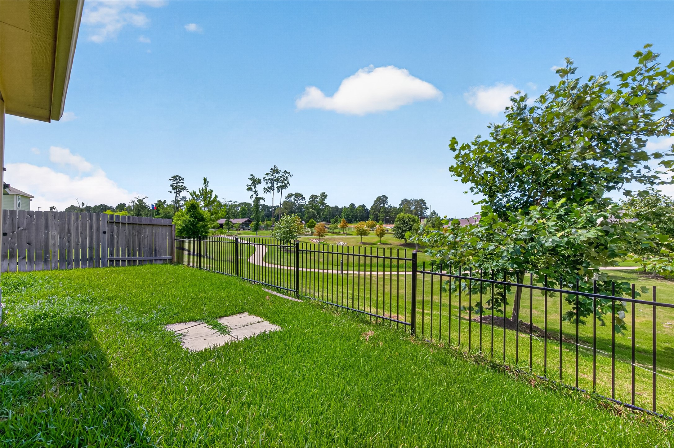 2526 Sturgeon Way Conroe, TX 77384 - Photo 38 of 49 This backyard features lush green grass, a metal fence offering unobstructed views of a scenic park with a walking path, and a wooden privacy fence on one side, creating a serene and inviting outdoor space.