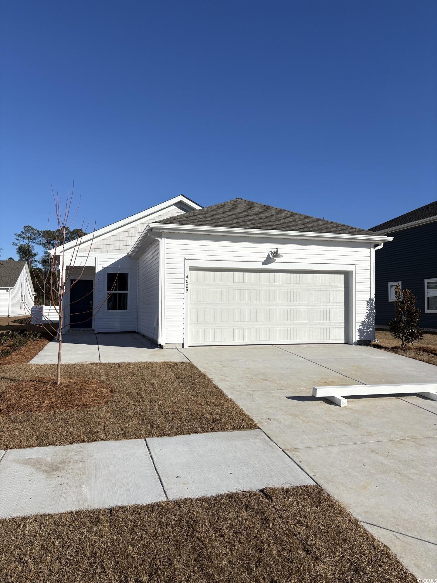 View of front of property featuring a front lawn, driveway, roof with shingles, and an attached garage