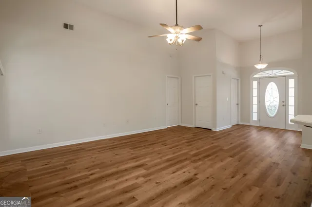 a view of an empty room with chandelier fan and wooden floor