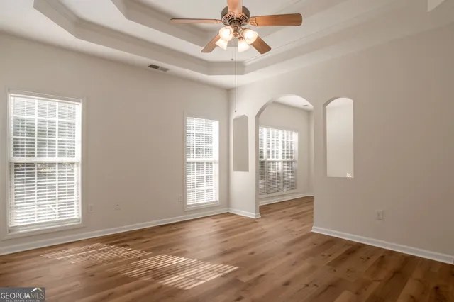 an empty room with wooden floor chandelier fan and windows