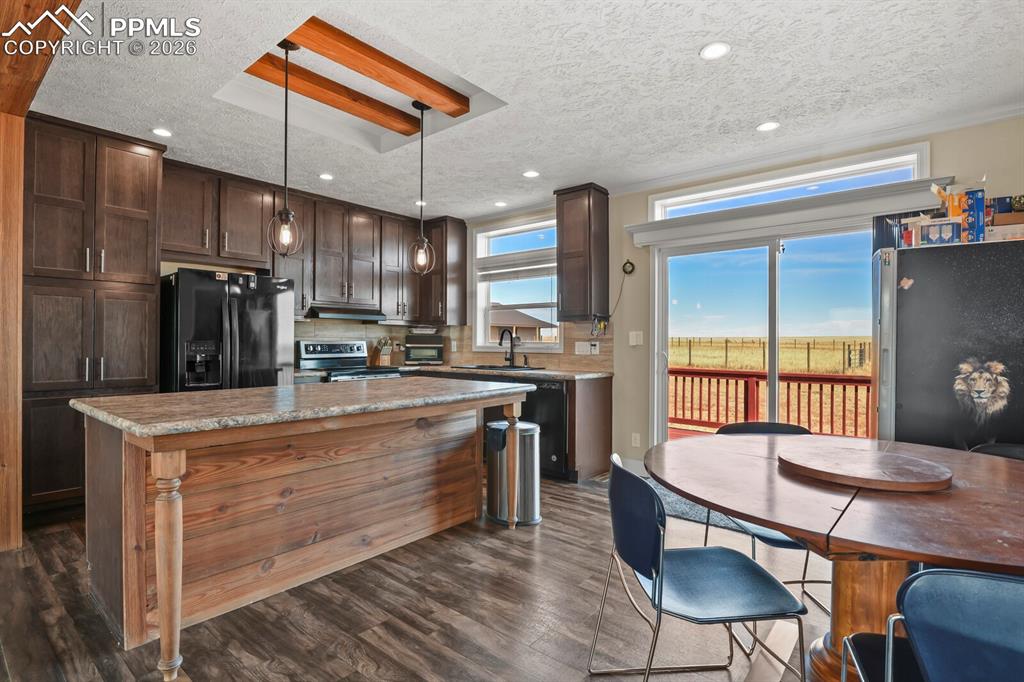 5895 Bar 10 Road Colorado Springs, CO 80928 - Photo 7 of 50 a kitchen with stainless steel appliances kitchen island granite countertop a table chairs in it and wooden floors