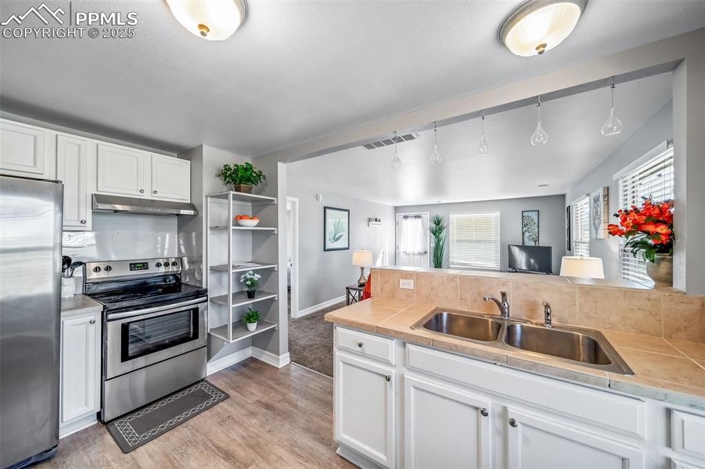 4586 East Best Road Larkspur, CO 80118 - Photo 46 of 50 Kitchen with white cabinets, stainless steel appliances, light wood-type flooring, and under cabinet range hood
