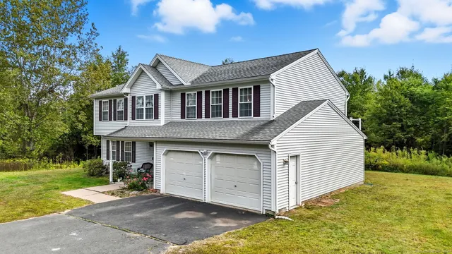 a view of a white house next to a yard with plants and large trees