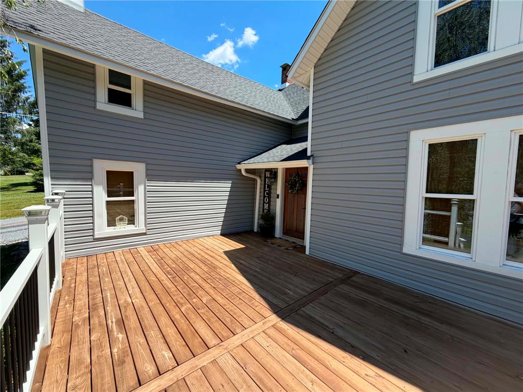164 Sand Spring Road Cresco, PA 18326 - Photo 11 of 60 A spacious wooden deck extends from a home with light gray siding under a clear blue sky.