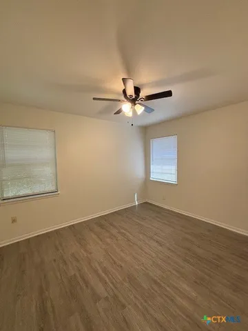 an empty room with wooden floor fan and windows
