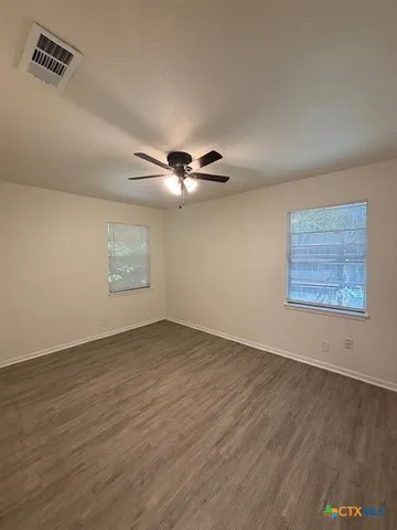an empty room with wooden floor fan and windows