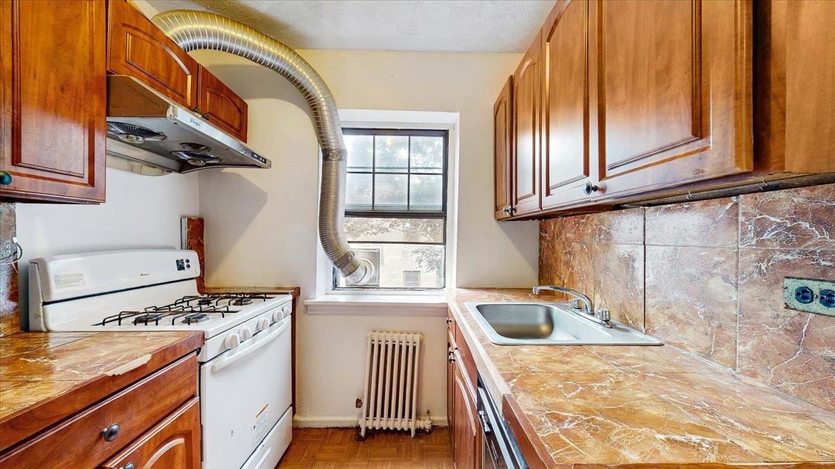 144-15 78th Road, Unit 3A Queens, NY 11367 - Photo 11 of 26 Kitchen with white range with gas stovetop, radiator, under cabinet range hood, backsplash, and dishwashing machine