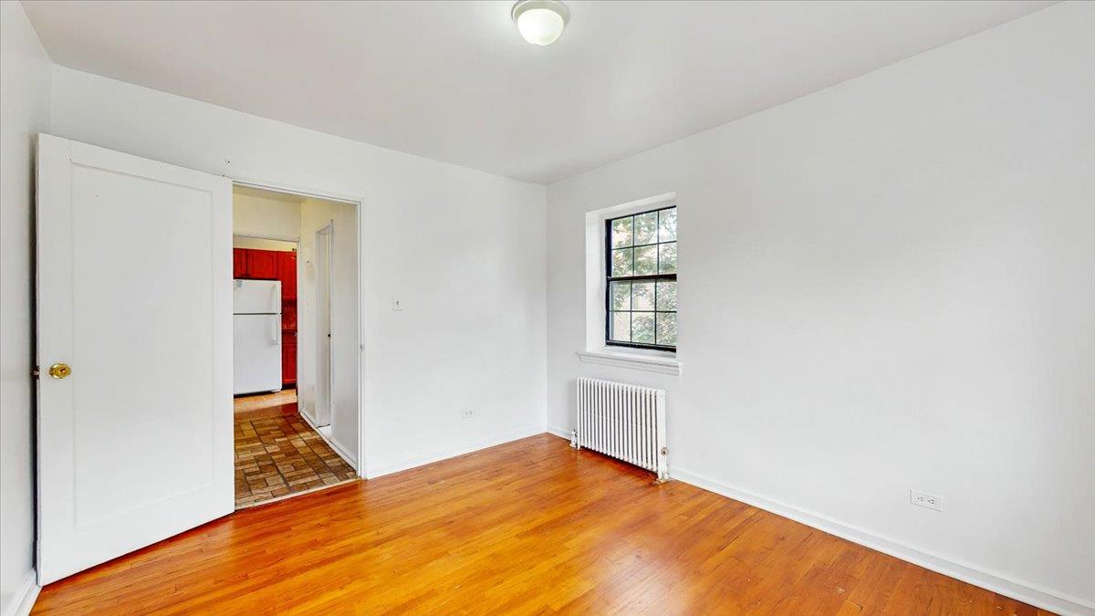 144-15 78th Road, Unit 3A Queens, NY 11367 - Photo 15 of 26 Empty room with radiator heating unit and light wood finished floors