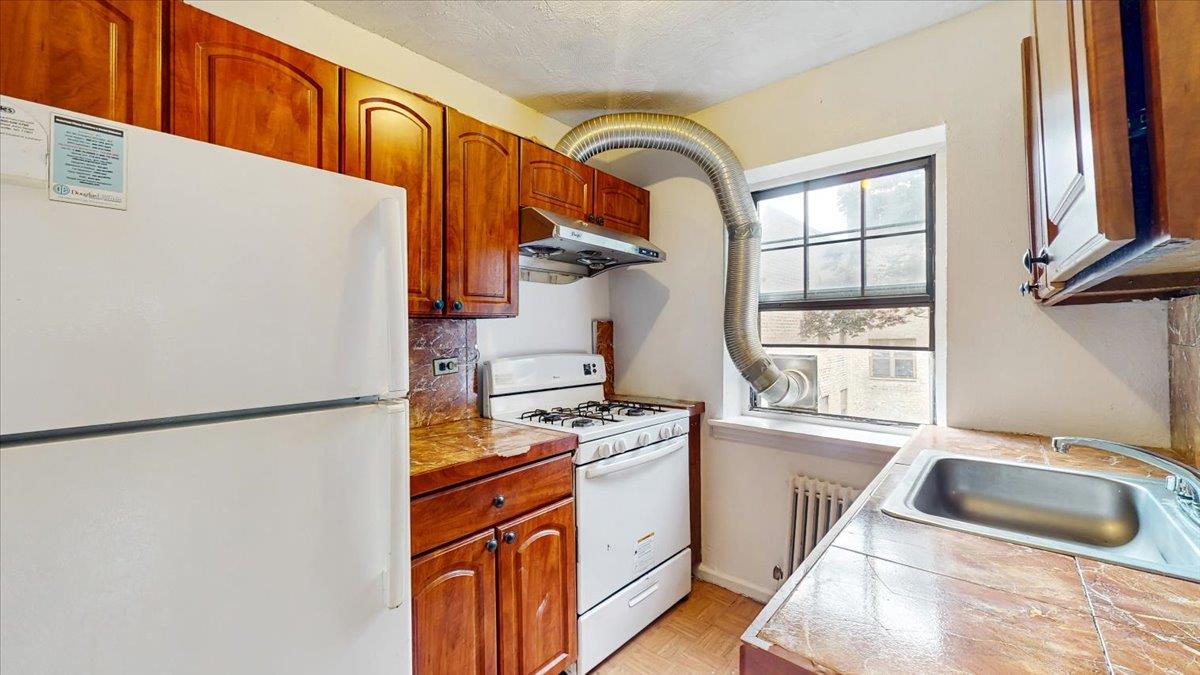 144-15 78th Road, Unit 3A Queens, NY 11367 - Photo 9 of 26 Kitchen featuring white appliances, under cabinet range hood, radiator heating unit, backsplash, and tile countertops
