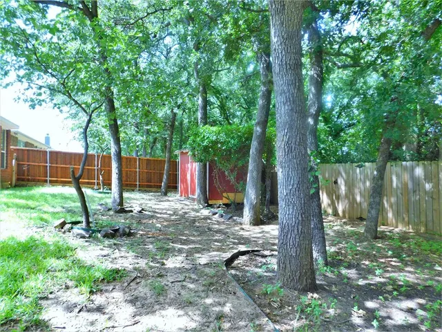 a backyard of a house with large trees and wooden fence