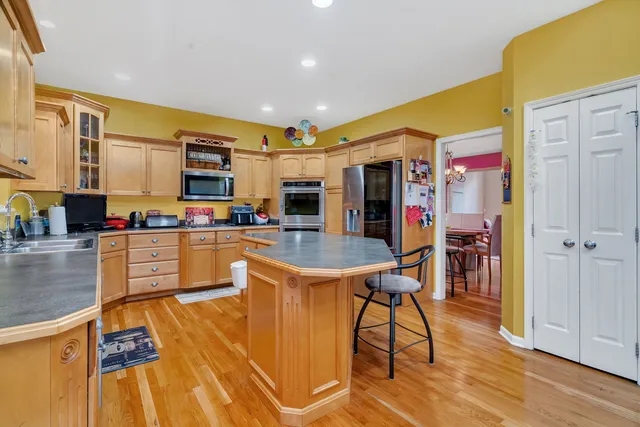 a kitchen with stainless steel appliances granite countertop a refrigerator a stove top oven and a dining table with wooden floor