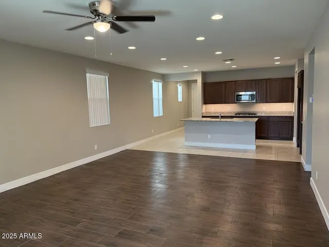 an empty room with wooden floor a ceiling fan and kitchen view