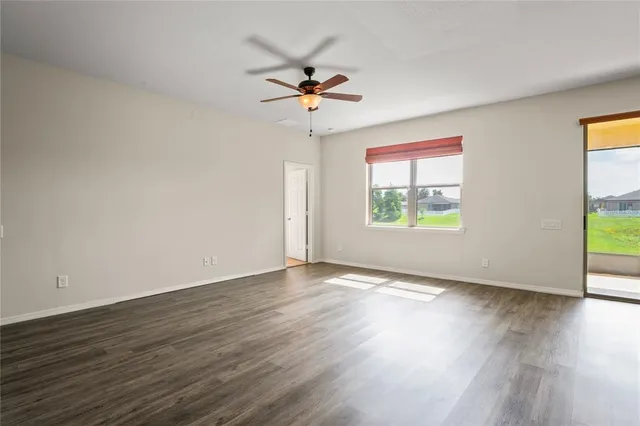 a view of an empty room with wooden floor and a ceiling fan