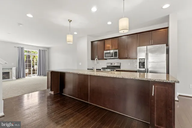 a kitchen with stainless steel appliances granite countertop a refrigerator a sink dishwasher a stove and a microwave oven on the wooden floor