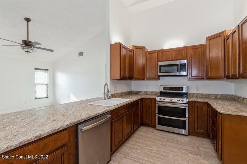 711 Montclair Road Northeast Palm Bay, FL 32905 - Photo 9 of 35 a kitchen with kitchen island granite countertop a sink dishwasher stove and microwave with wooden cabinets