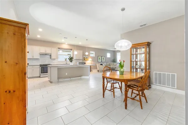 a dining hall with stainless steel appliances kitchen island granite countertop a dining table chairs and a refrigerator