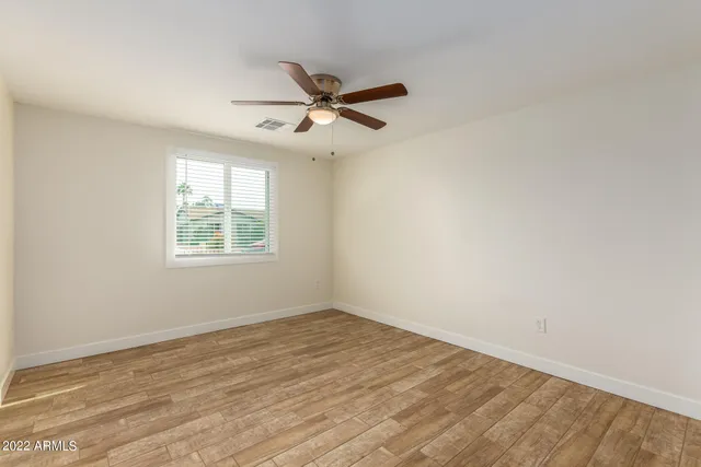 an empty room with wooden floor ceiling fan and windows