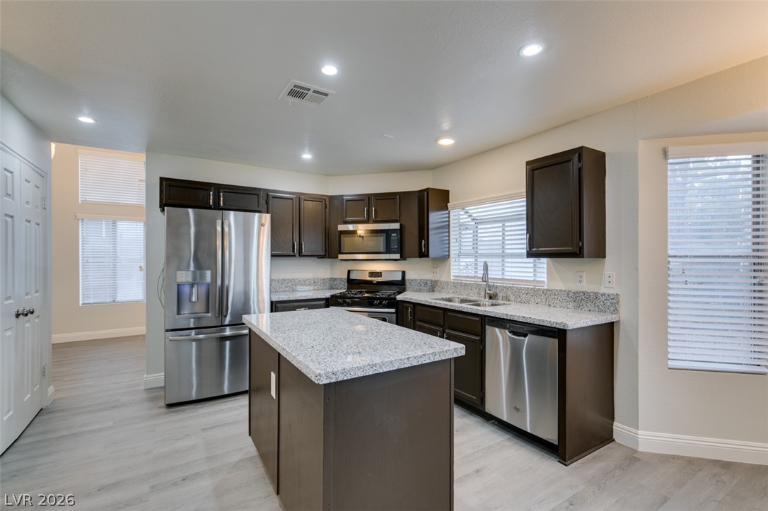 1738 Toltec Circle Henderson, NV 89014 - Photo 3 of 46 A contemporary kitchen features dark cabinetry, light granite counters, and stainless steel appliances, all set on sleek grey flooring.