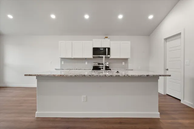 a kitchen with stainless steel appliances granite countertop a sink a stove a microwave a sink a refrigerator and white cabinets