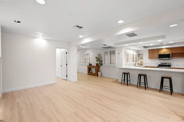 a view of an empty room with kitchen and window
