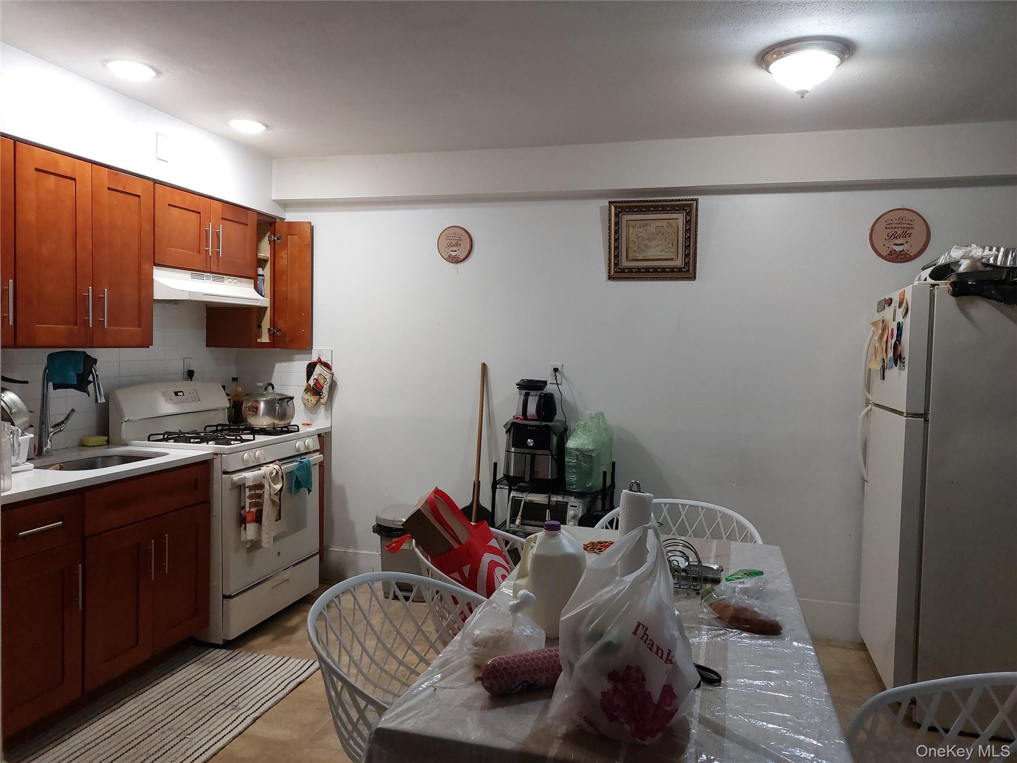 108-19 48th Avenue Queens, NY 11368 - Photo 20 of 21 Kitchen with white appliances, decorative backsplash, brown cabinetry, and under cabinet range hood