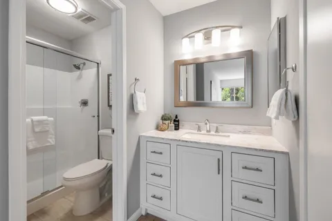 a bathroom with a toilet a sink a glass door a shower a mirror a vanity and window