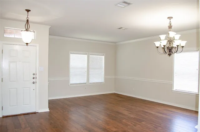 an empty room with wooden floor chandelier and windows
