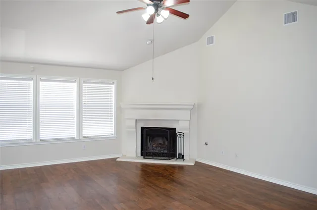 an empty room with wooden floor fireplace and windows