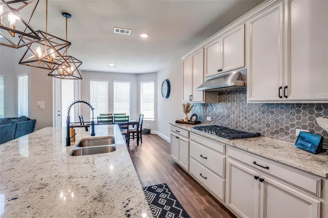 a kitchen with stainless steel appliances granite countertop a stove a sink dishwasher and white cabinets with wooden floor