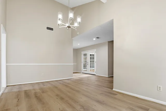 an empty room with wooden floor chandelier fan and windows