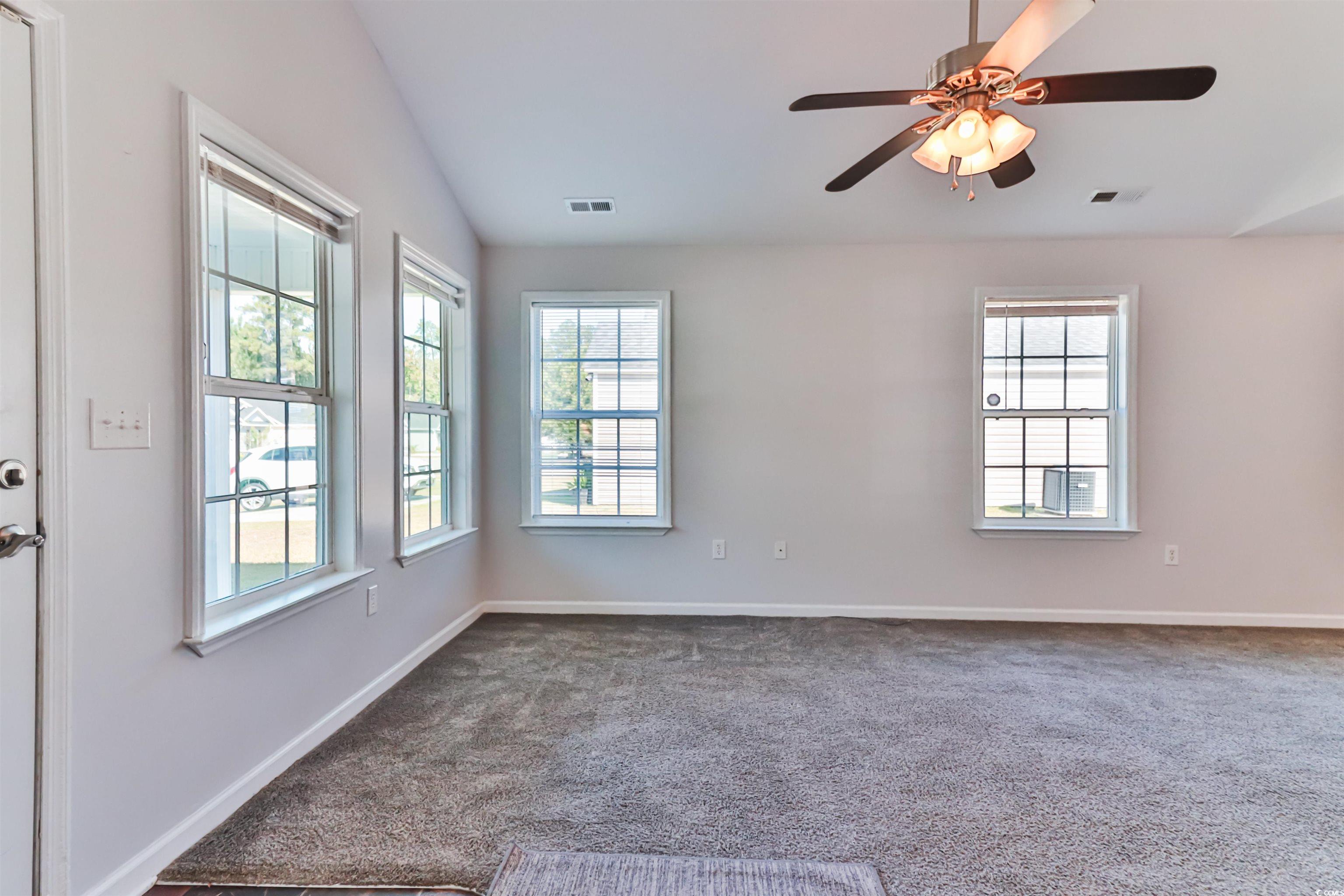 Carpeted spare room with ceiling fan and vaulted c