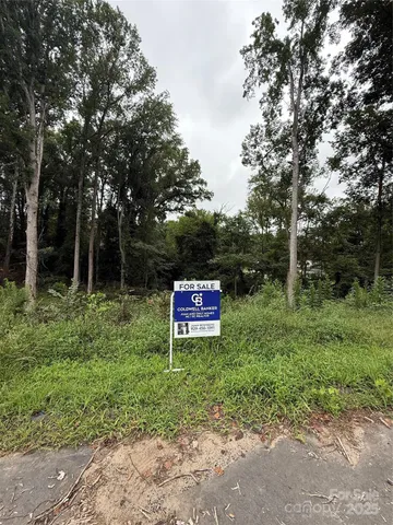 a sign that is sitting in a big yard with large trees