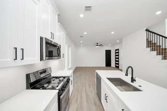 a kitchen with stainless steel appliances a sink dishwasher a stove and a microwave oven with white cabinets