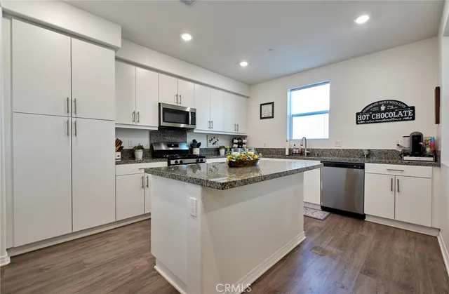 a kitchen with granite countertop a stove top oven a sink a refrigerator and white cabinets with wooden floor