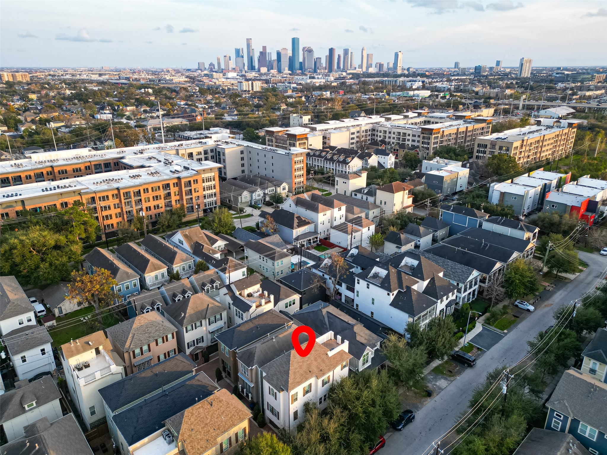 620 Rutland Street, Unit A Houston, TX 77007 - Photo 36 of 46 This photo showcases a residential area with a mix of modern townhouses and apartment buildings. The neighborhood is near a city skyline, indicating proximity to downtown. The highlighted house is centrally located, surrounded by greenery and well-maintained streets.