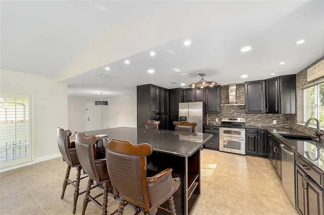 a kitchen with stainless steel appliances kitchen island granite countertop a stove a sink a refrigerator and a dining table with wooden floor