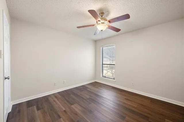 an empty room with wooden floor fan and windows
