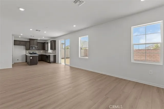 an empty room with wooden floor kitchen view and a window
