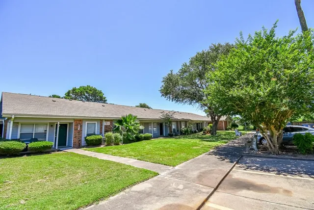 a view of house in front of a big yard with potted plants and large trees