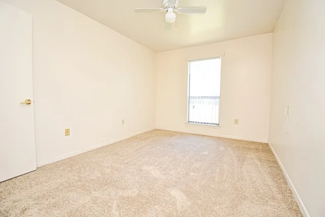 an empty room with a chandelier fan and windows