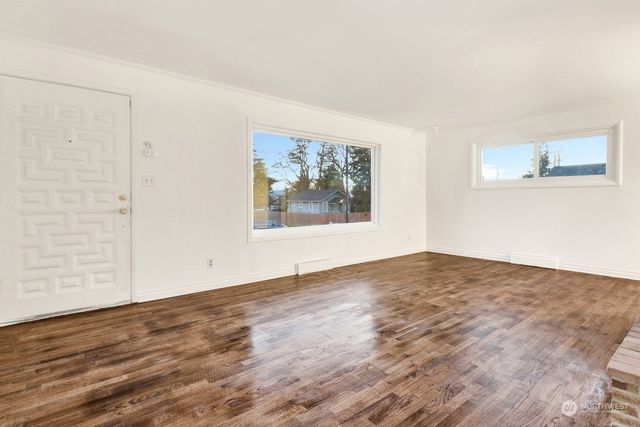 a view of an empty room with wooden floor and window
